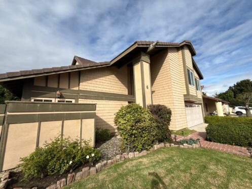 Cream-colored two-story residential home with taupe trim, shake siding, and dark garage doors in Irvine, CA exterior paint failing moisture damage