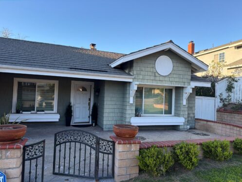 A beautifully painted residential exterior featuring light green shingle siding, crisp white trim, and a welcoming white front door. Exterior Paint Problems